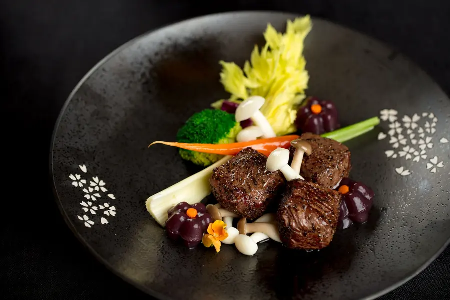 Beef medallions with vegetables and edible flowers on black stoneware